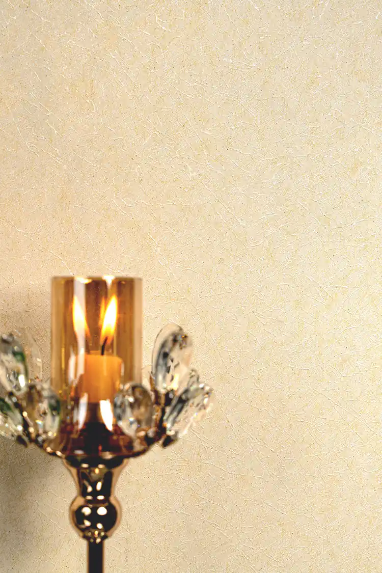 Warm close-up of cream silk wallpaper with lit candle in crystal holder showing soft shimmer