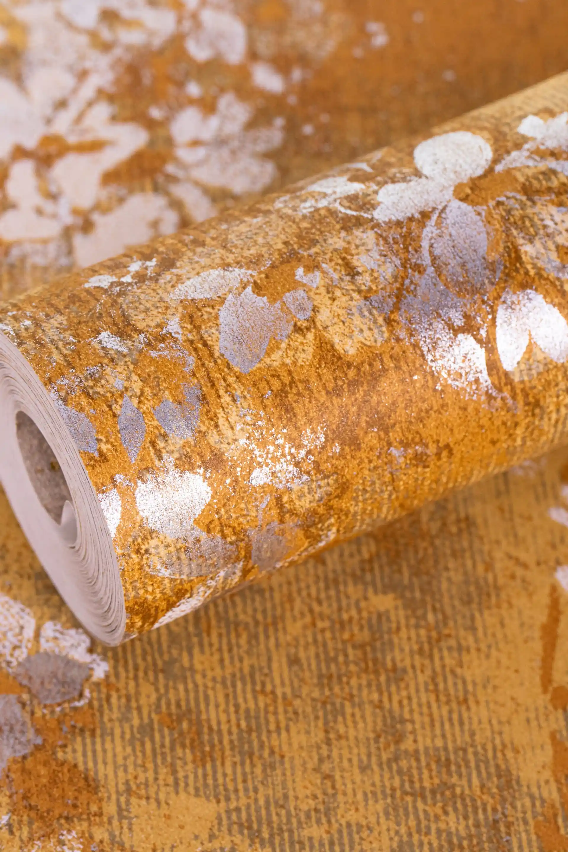 Full roll of rustic gold blossom wallpaper with pale grey floral pattern on a warm amber base