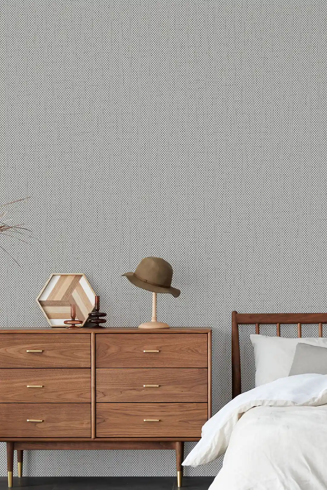 Grey grasscloth wallpaper in a minimalist bedroom with walnut dresser, hat, and white bedding