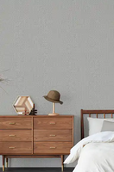 Grey grasscloth wallpaper in a minimalist bedroom with walnut dresser, hat, and white bedding