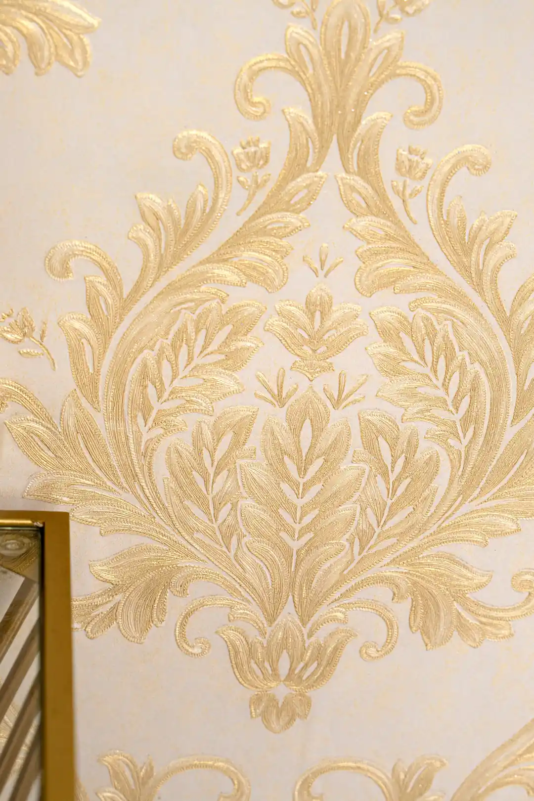 Detailed view of single embossed gold acanthus leaf damask medallion on cream wallpaper