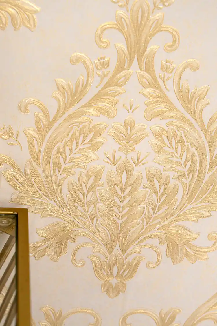 Detailed view of single embossed gold acanthus leaf damask medallion on cream wallpaper