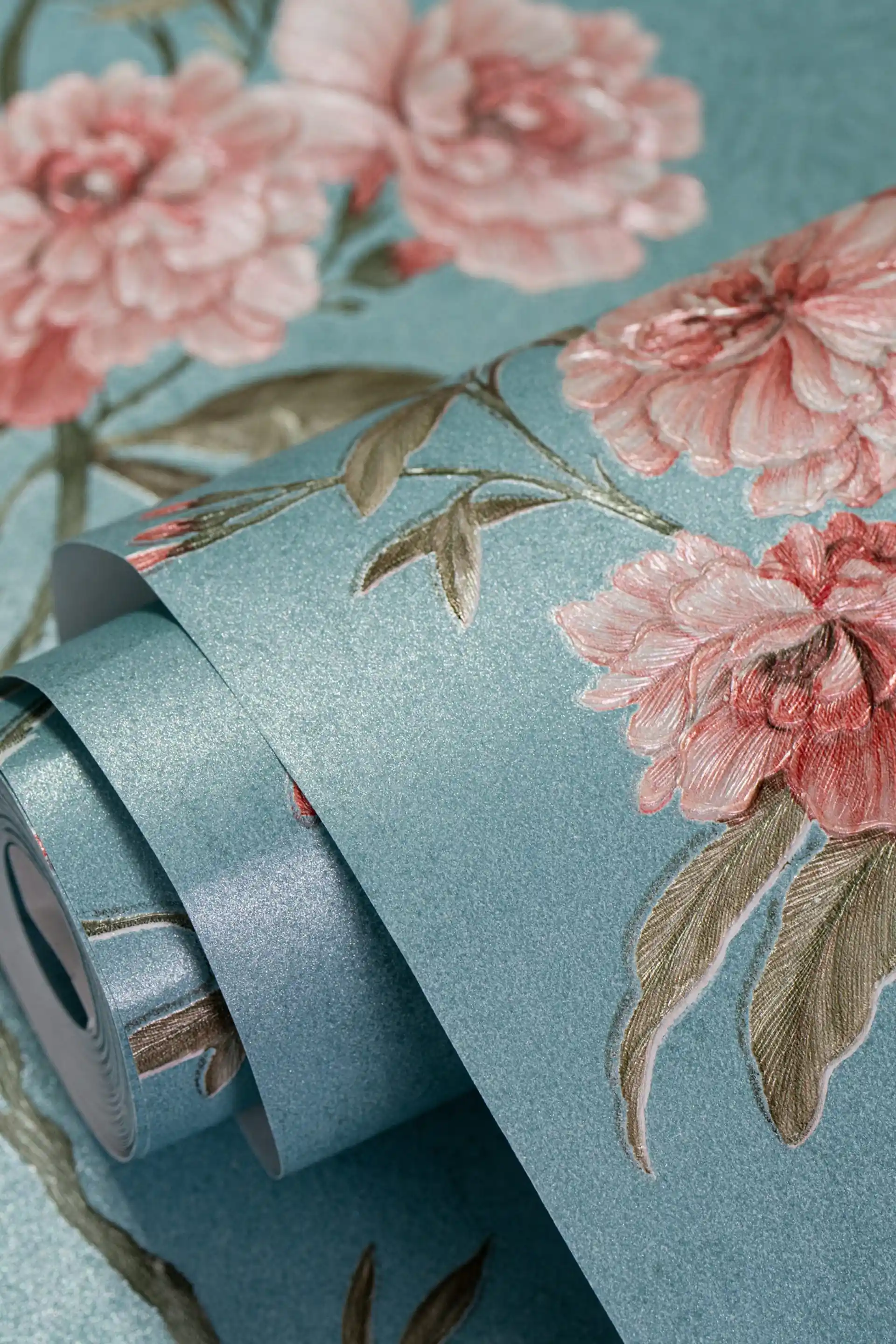 Wallpaper roll with pink peony roses on a teal blue shimmer base showing floral detail