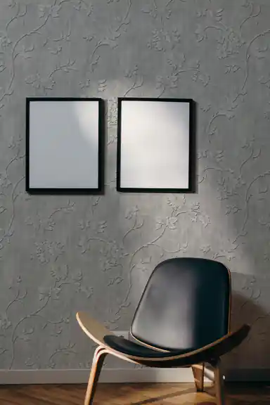 Modern living room with silver floral vine embossed wallpaper, dark leather shell chair, and blank white frames