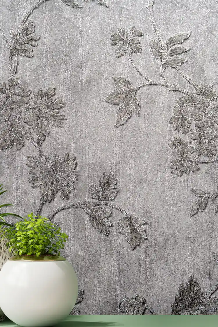 Close-up of silver embossed floral vine and leaves on grey wallpaper with green plant accent