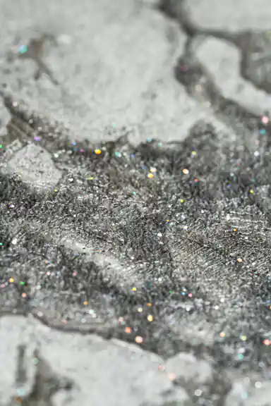 Extreme close-up macro of holographic glitter particles embedded in grey marble wallpaper texture