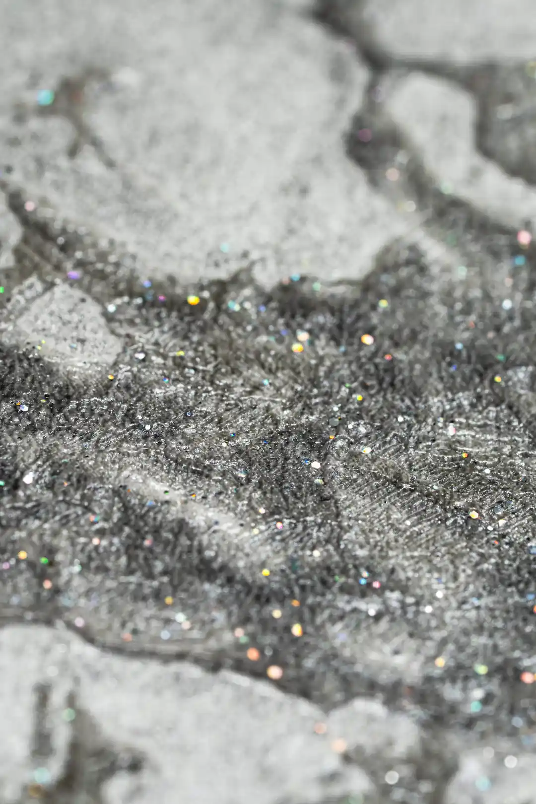 Extreme close-up macro of holographic glitter particles embedded in grey marble wallpaper texture