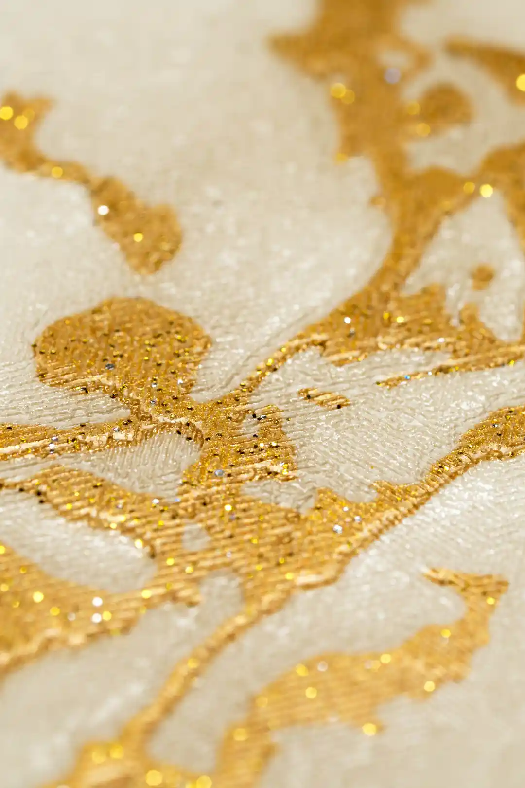 Extreme close-up of gold veining and shimmer detail on cream marble wallpaper surface
