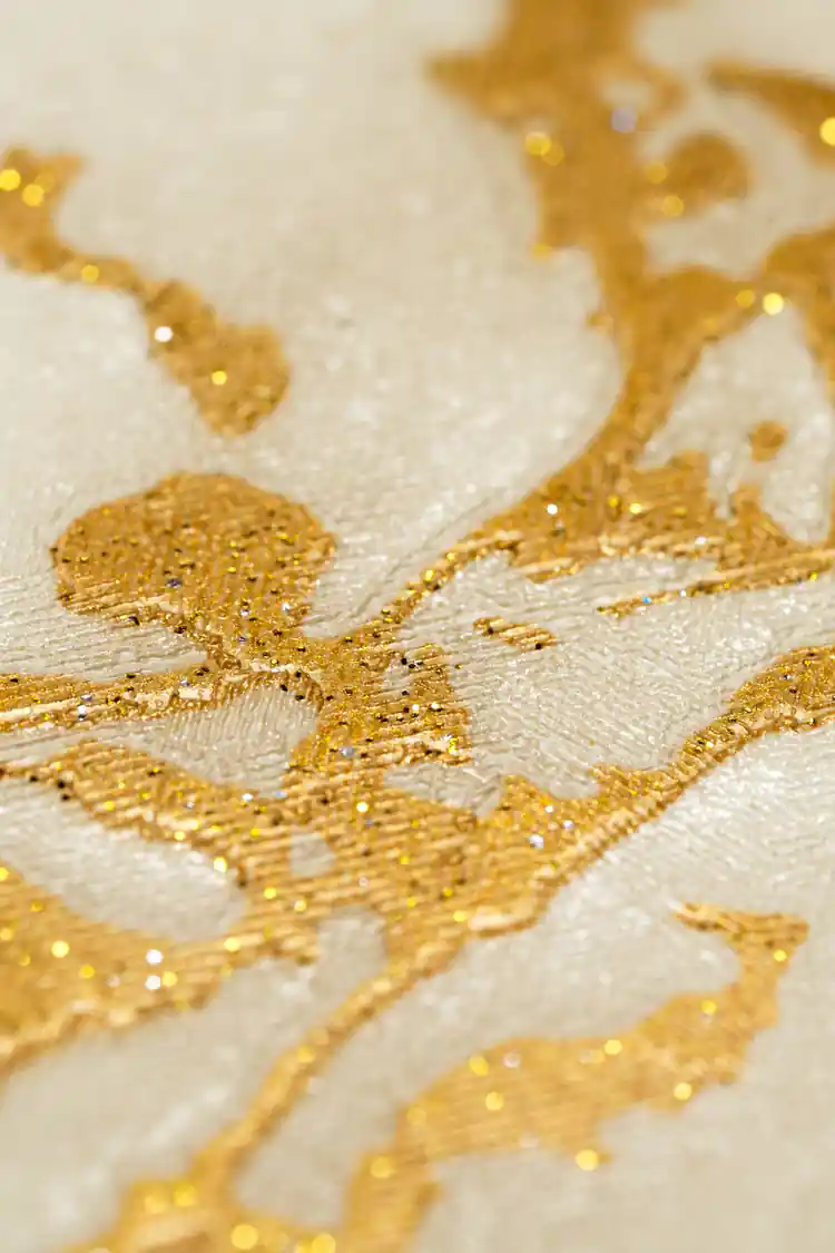 Extreme close-up of gold veining and shimmer detail on cream marble wallpaper surface
