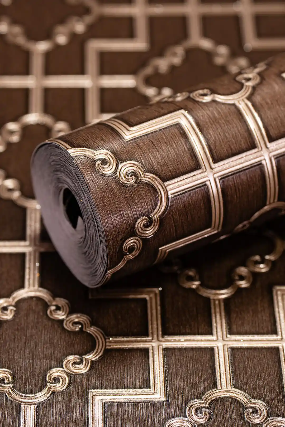 Rolled brown geometric trellis wallpaper showing embossed pattern with gold scroll accents