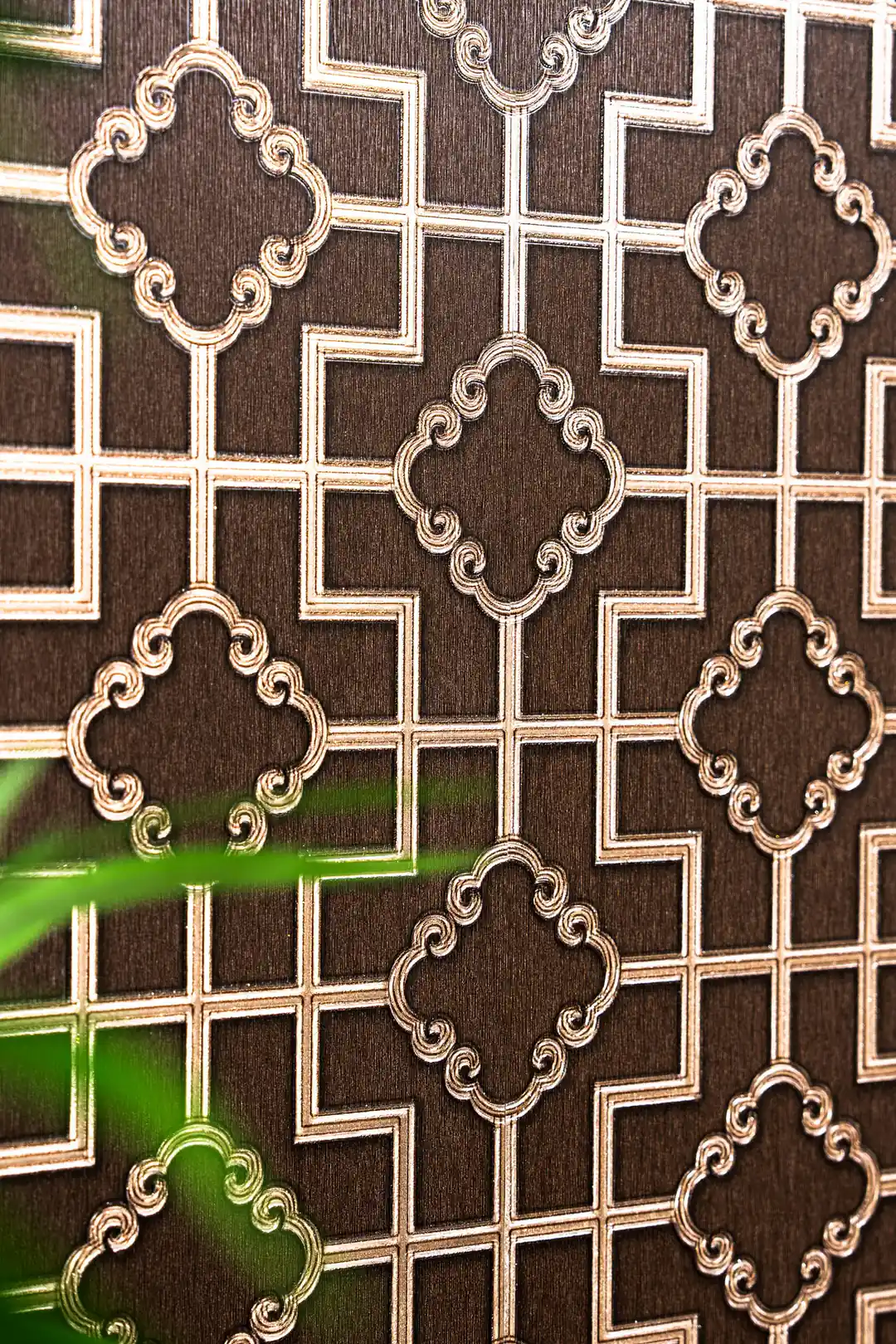 Angled view of embossed gold metallic quatrefoil pattern on brown geometric lattice wallpaper
