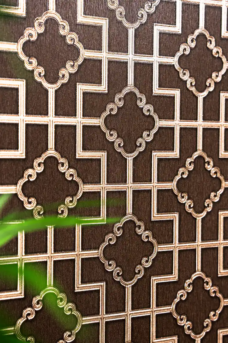 Angled view of embossed gold metallic quatrefoil pattern on brown geometric lattice wallpaper