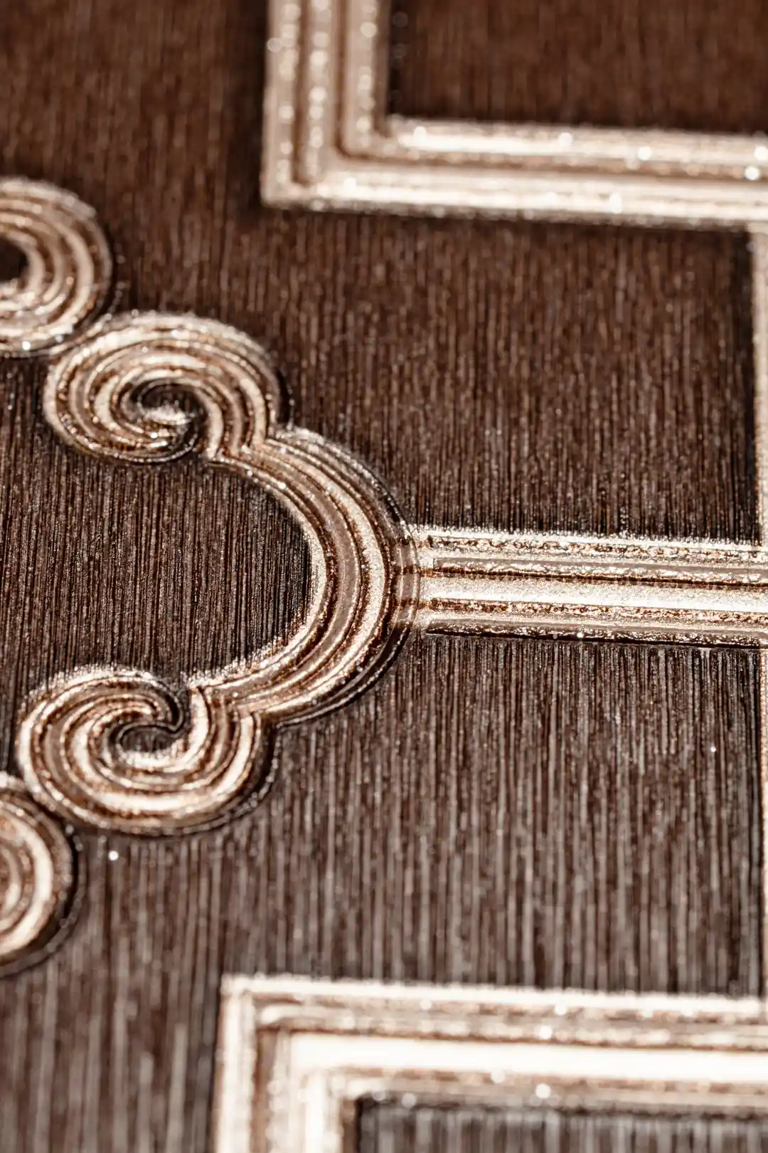 Extreme close-up of raised gold metallic scroll detail at trellis intersection on brown wallpaper