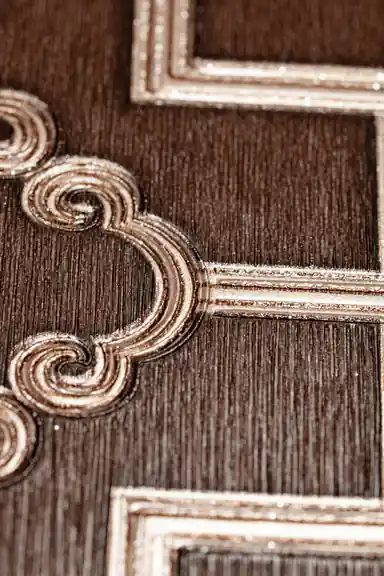 Extreme close-up of raised gold metallic scroll detail at trellis intersection on brown wallpaper