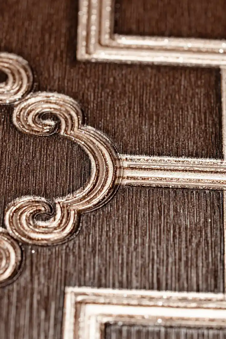 Extreme close-up of raised gold metallic scroll detail at trellis intersection on brown wallpaper