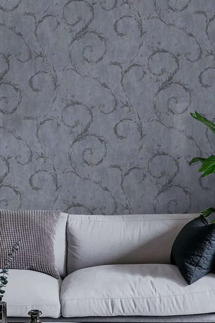 Living room with grey leaf swirl wallpaper behind a white sofa with cushions and green plant