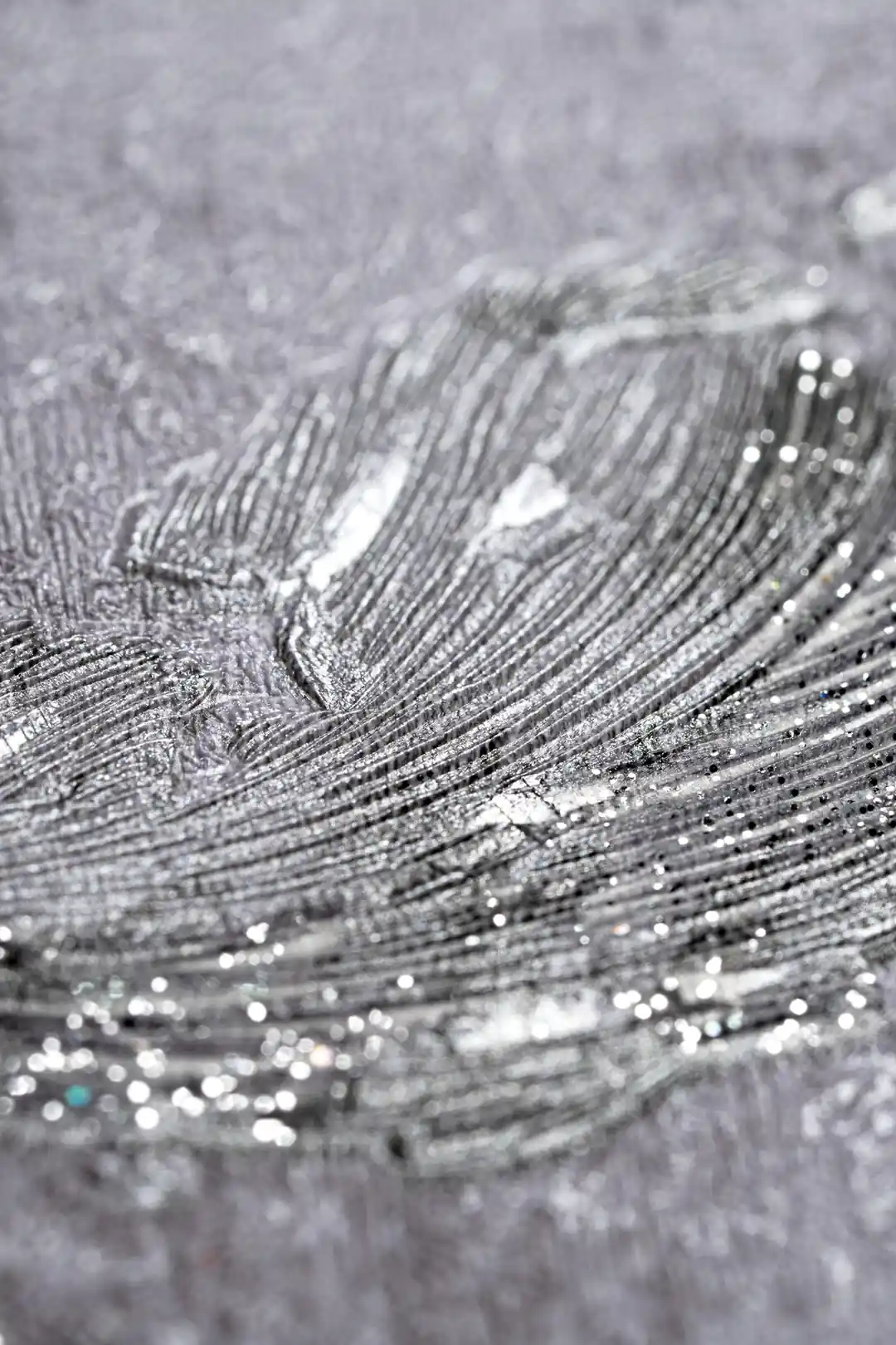 Extreme close-up macro of silver metallic scroll texture showing glitter shimmer on grey wallpaper