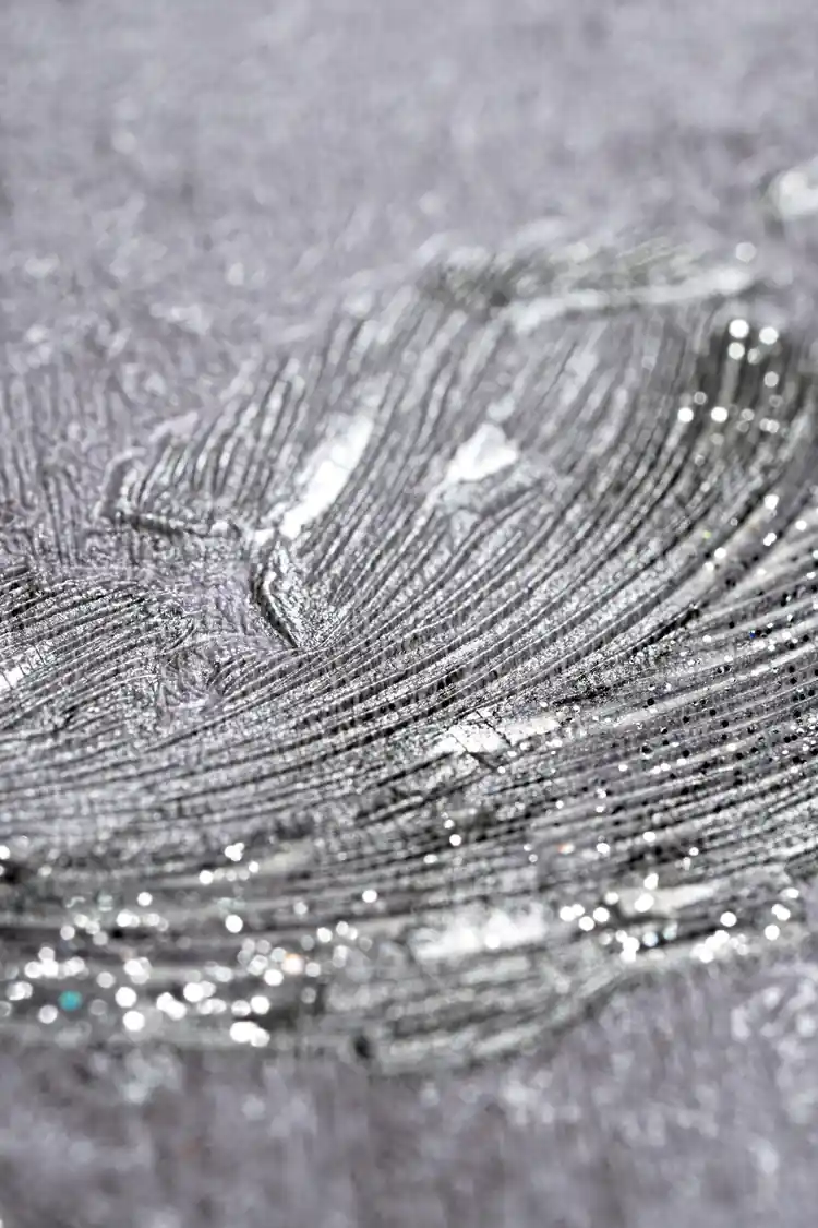 Extreme close-up macro of silver metallic scroll texture showing glitter shimmer on grey wallpaper