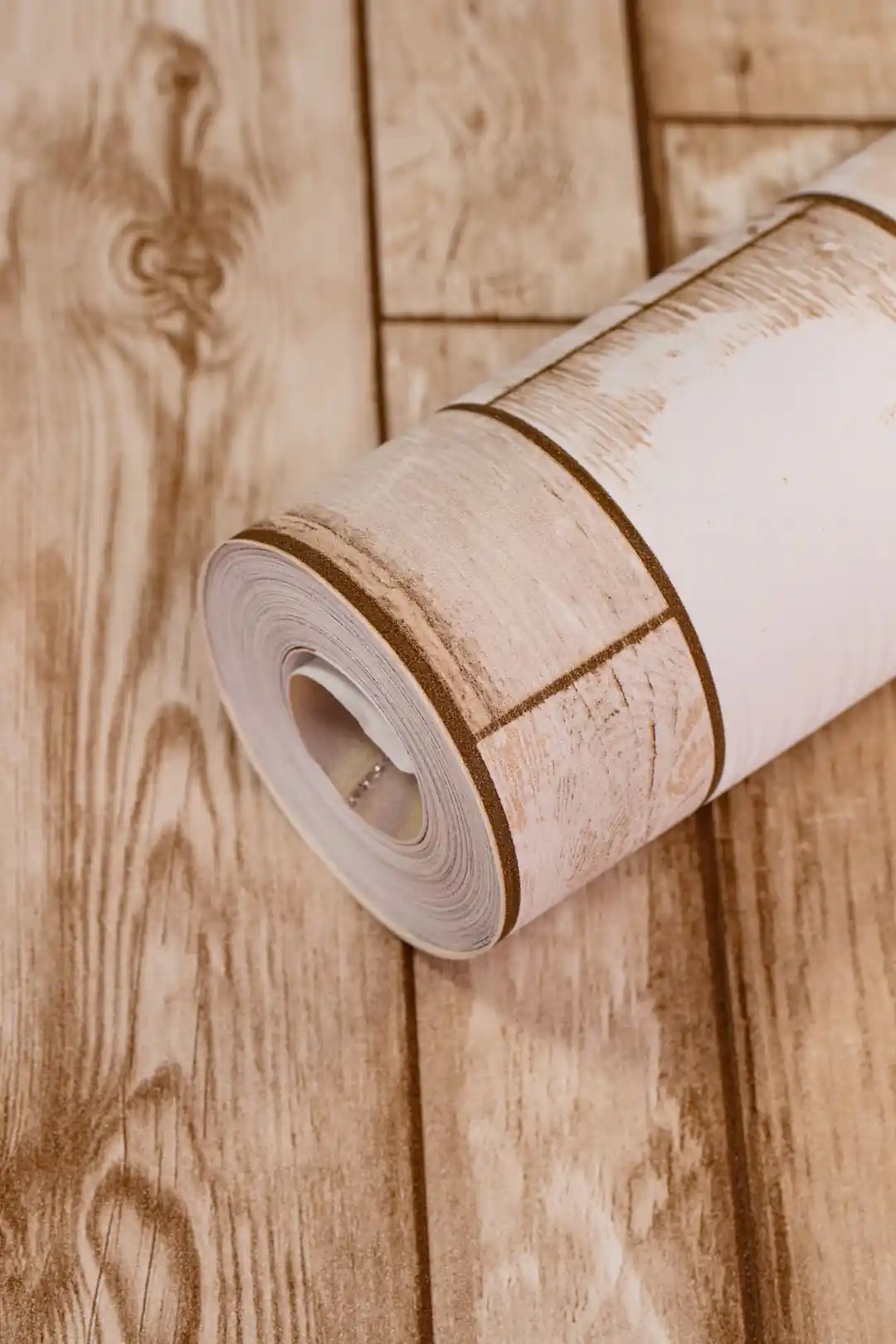 Wallpaper roll showing natural beige wood grain pattern with plank lines on warm background