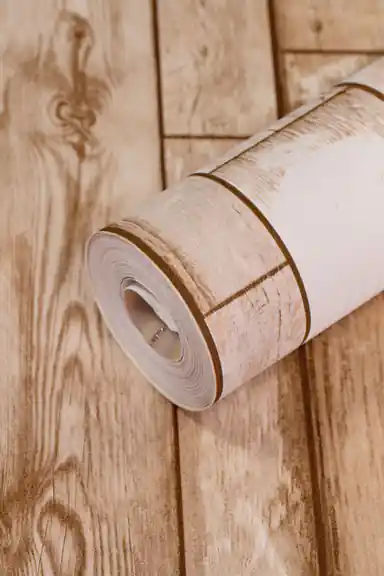 Wallpaper roll showing natural beige wood grain pattern with plank lines on warm background