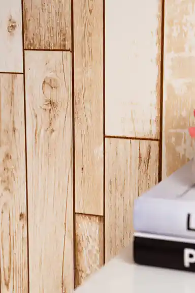 Close-up of installed beige wood plank wallpaper showing natural knot and grain detail with books