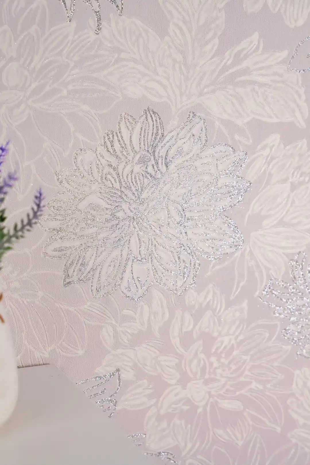 Close-up of a single silver glitter chrysanthemum bloom on soft pink embossed wallpaper