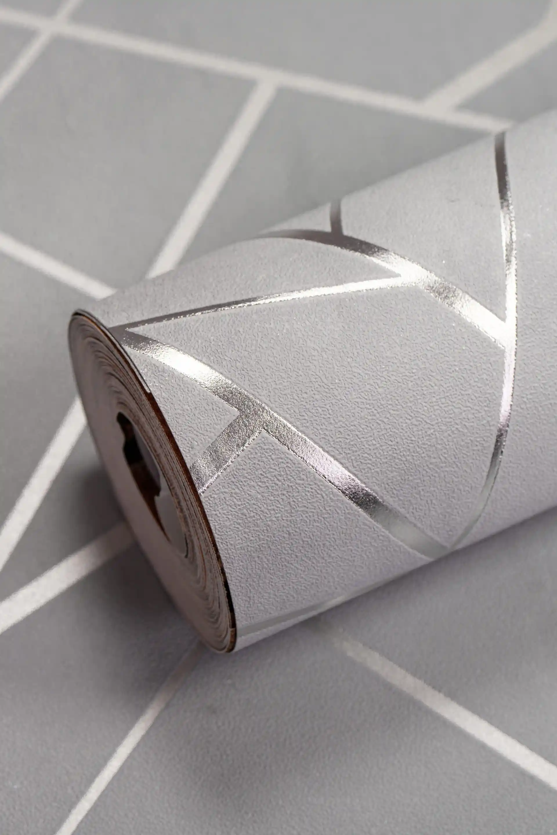 Gray geometric wallpaper roll with metallic silver angular lines on a matte grey background