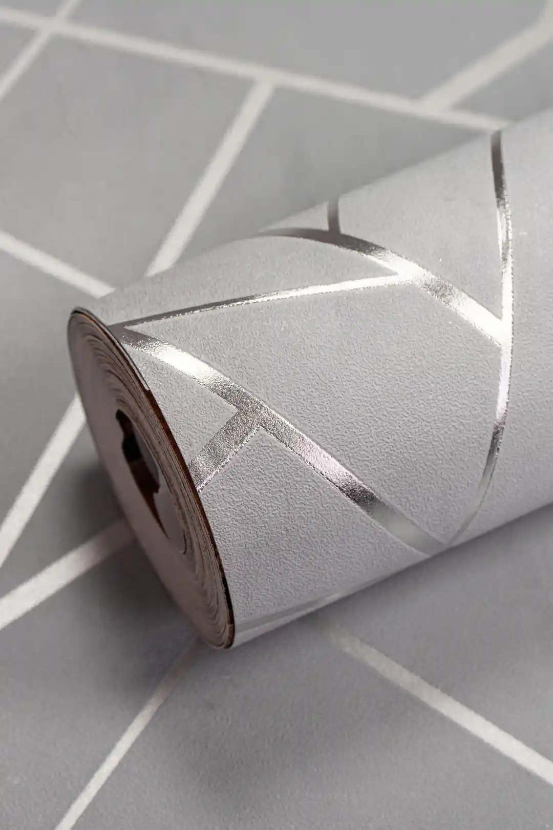 Gray geometric wallpaper roll with metallic silver angular lines on a matte grey background