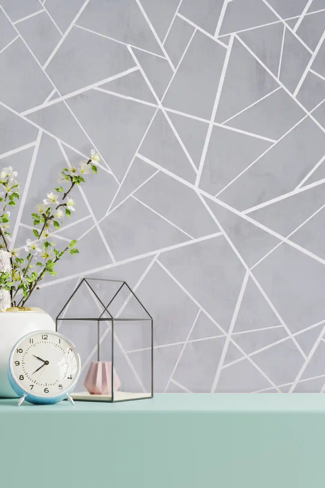 Installed gray abstract geometric wallpaper behind a mint shelf with a clock, flowers, and glass terrarium