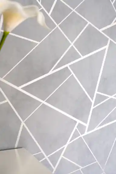 Close-up of gray wallpaper showing intersecting metallic silver geometric lines and a calla lily