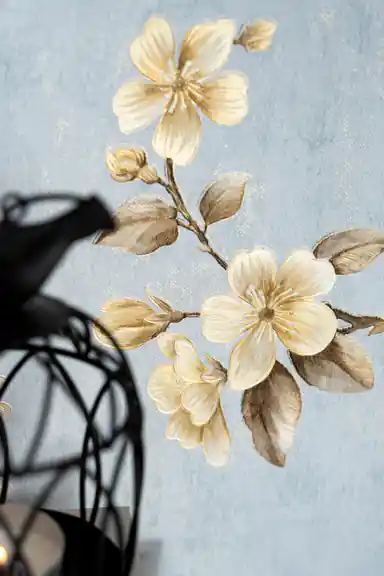 Close-up of golden cherry blossom flowers and brown branches on blue wallpaper with a decorative lantern