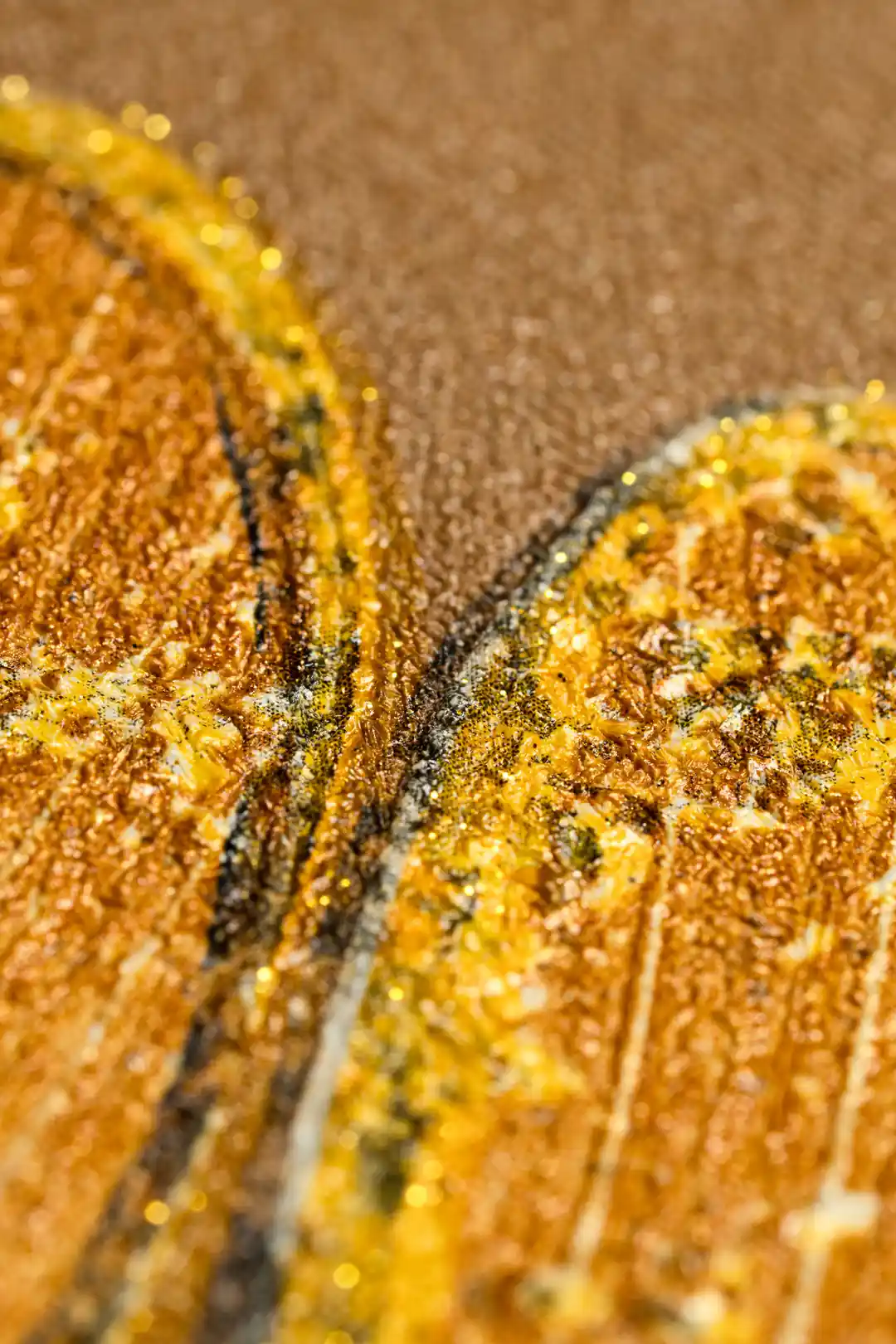 Extreme macro of golden-orange ginkgo leaf texture showing glitter particles and embossed vein details