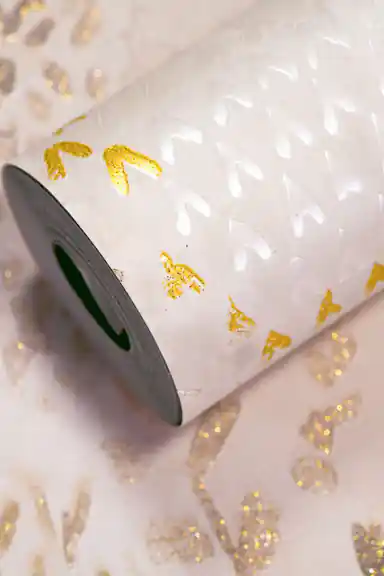Cream wallpaper roll with small gold glitter coral sprigs and embossed teardrop texture on a soft cream base