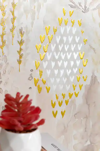 Close-up of gold and white chevron hearts arranged in diamond pattern with glitter accents on cream watercolor wallpaper