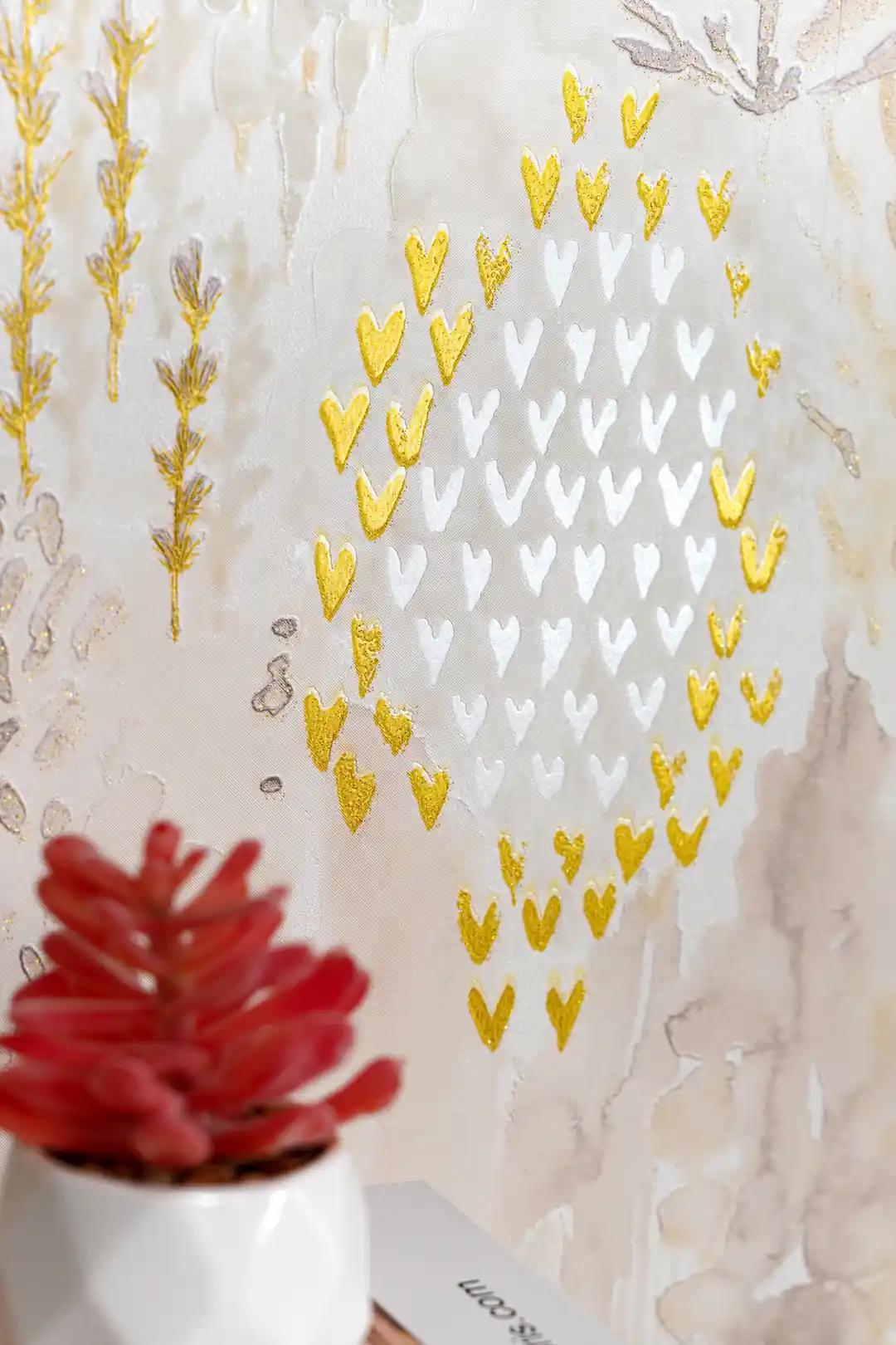 Close-up of gold and white chevron hearts arranged in diamond pattern with glitter accents on cream watercolor wallpaper