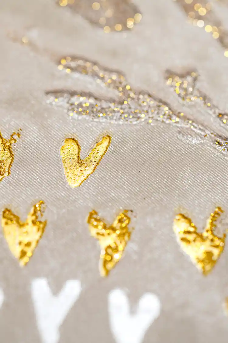 Extreme macro of gold glitter hearts and silver leaf shimmer on textured cream wallpaper surface