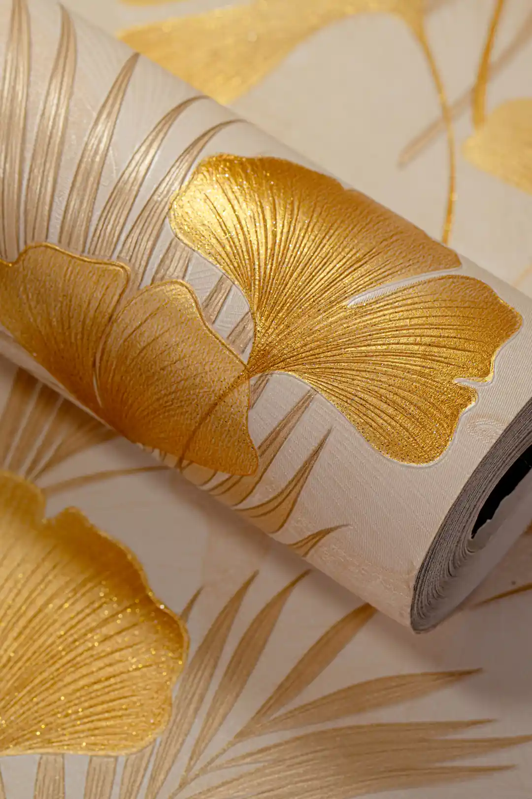 Metallic gold ginkgo leaf wallpaper roll with large fan-shaped leaves and palm fronds on a cream background