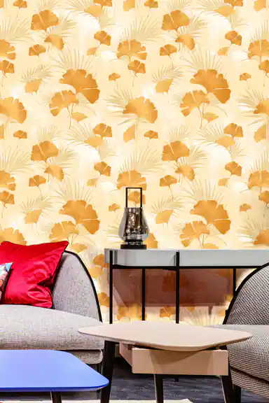 Living room with gold ginkgo wallpaper on cream behind a grey sofa with red cushion and modern furniture