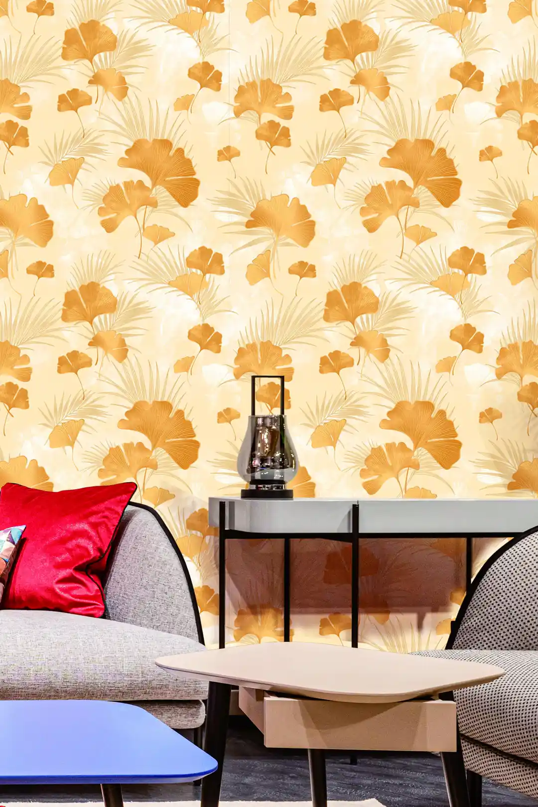Living room with gold ginkgo wallpaper on cream behind a grey sofa with red cushion and modern furniture
