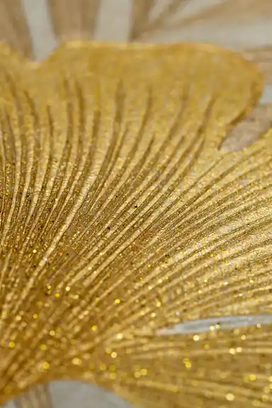 Extreme close-up of a gold ginkgo leaf showing fine glitter veins and radial texture on cream wallpaper