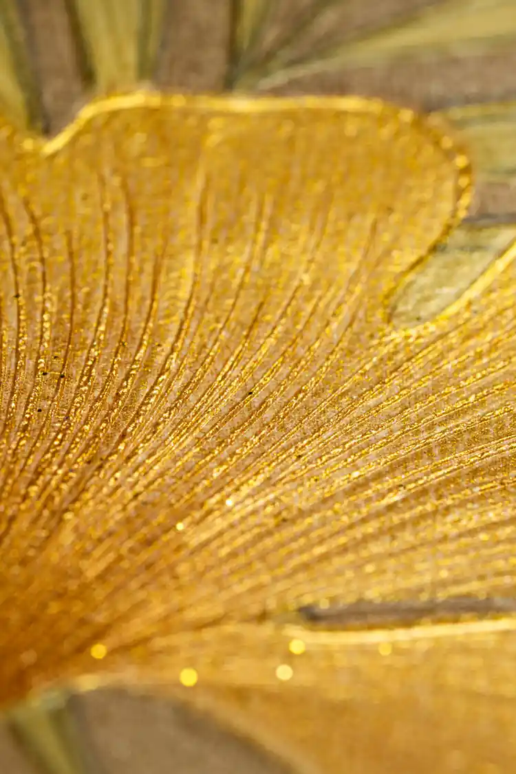 Extreme macro of embossed gold ginkgo leaf with radiating veins and glitter detail on brown textured wallpaper