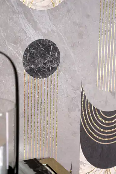 Close-up of black marble circle with gold glitter chains and curved arch motifs on grey wallpaper