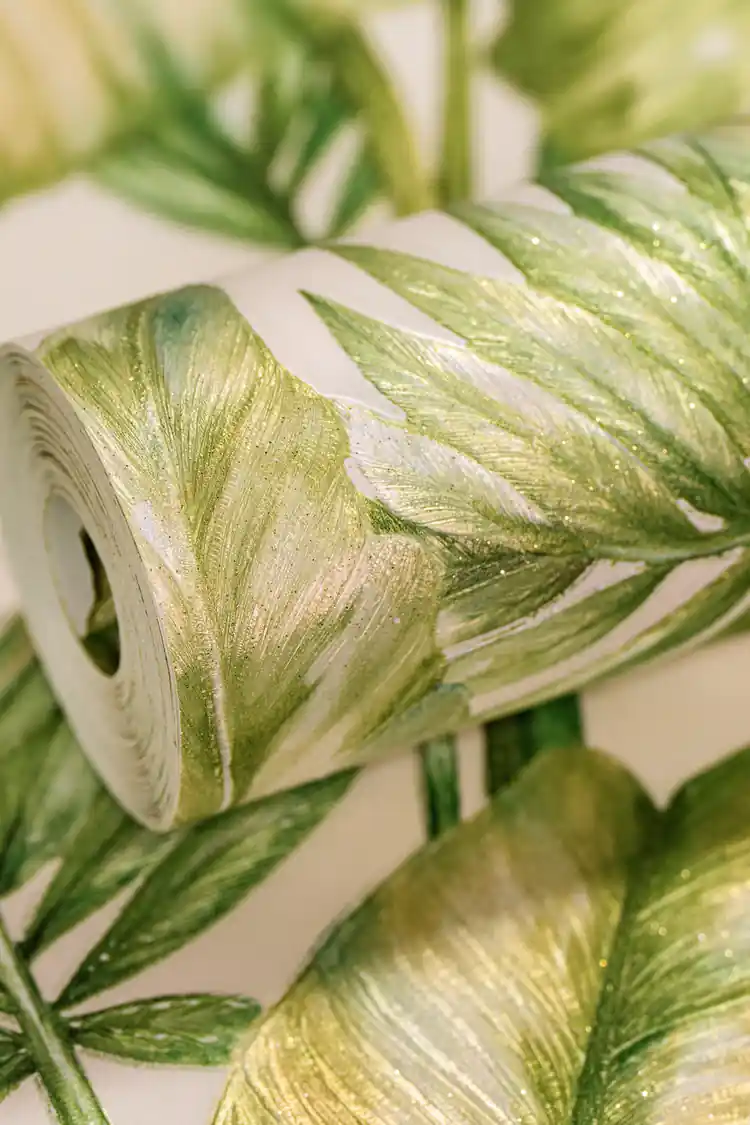 Green tropical wallpaper roll with lush monstera and palm leaves featuring gold sparkle on cream base