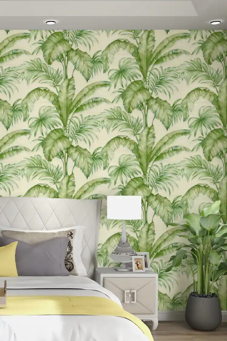 Tropical bedroom with green palm and monstera wallpaper behind a grey bed with yellow throw and plants