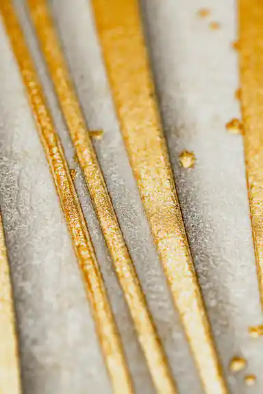 Extreme close-up of metallic gold wave stripes showing glitter texture and shimmer on cream wallpaper