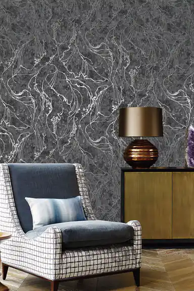 Living room with dark grey abstract wallpaper behind a plaid wing chair, brass lamp, and wooden sideboard