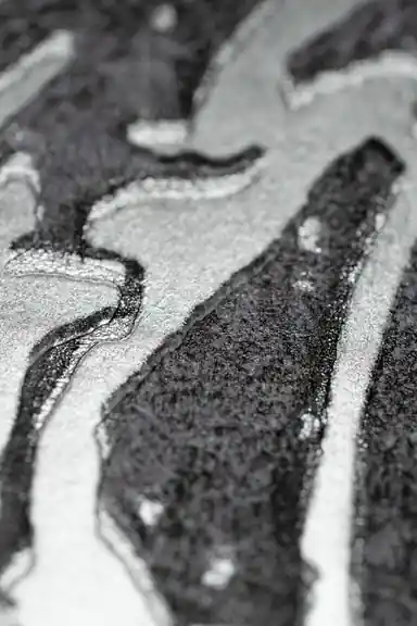 Extreme macro of silver and black abstract swirl texture showing metallic shimmer on grey wallpaper
