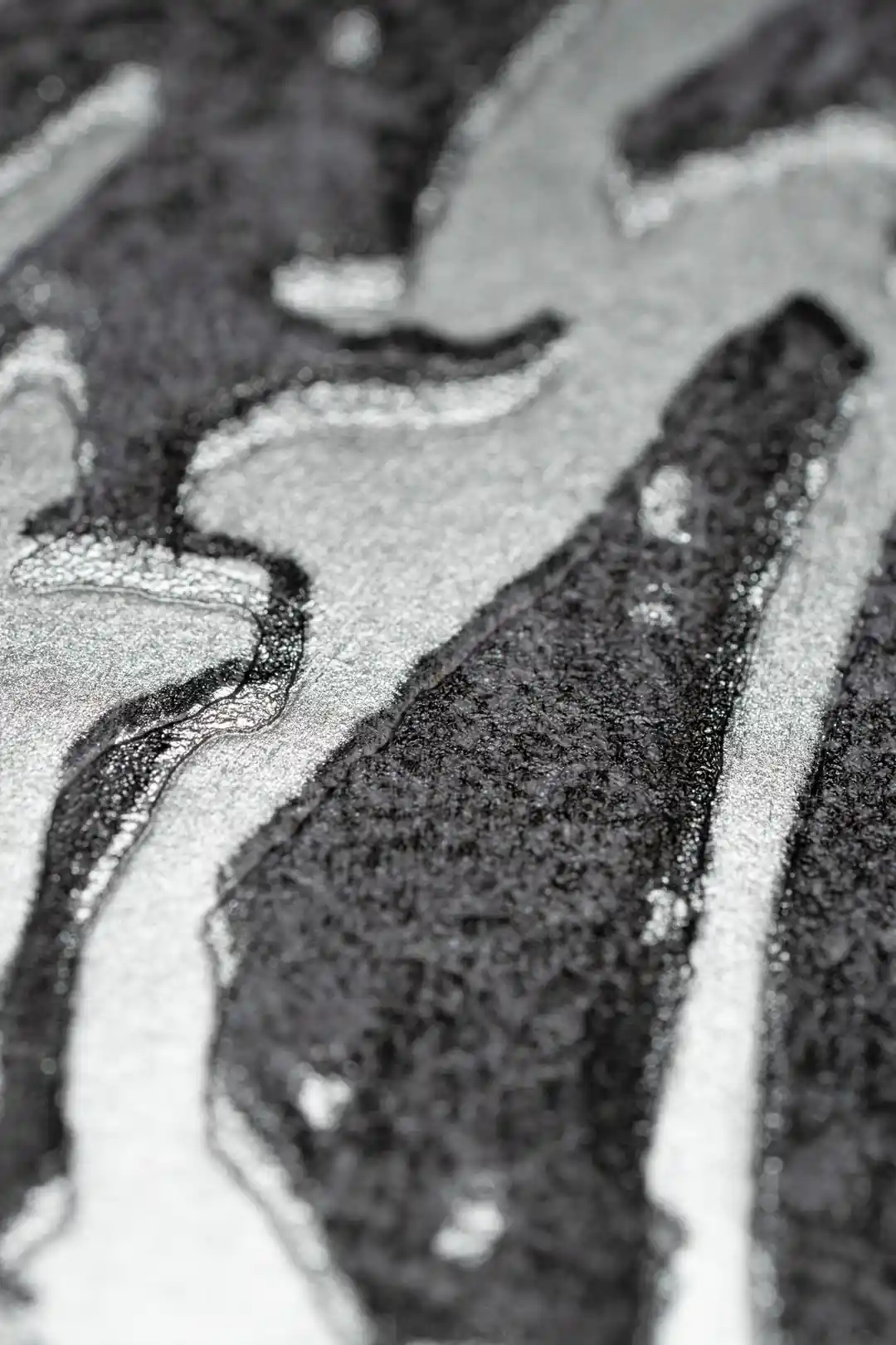 Extreme macro of silver and black abstract swirl texture showing metallic shimmer on grey wallpaper