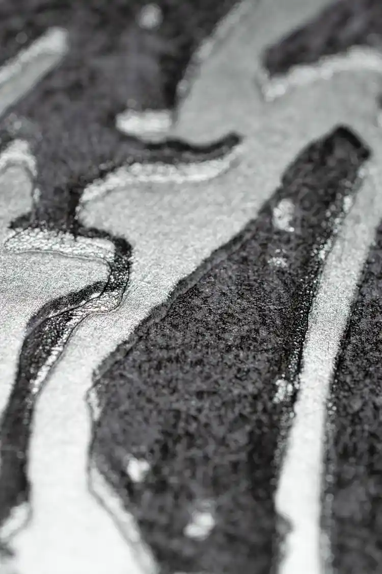 Extreme macro of silver and black abstract swirl texture showing metallic shimmer on grey wallpaper
