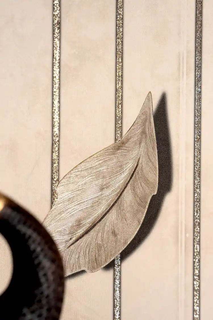 Close-up of a single embossed gold-beige leaf with shadow effect and glitter stripe detail on cream wallpaper